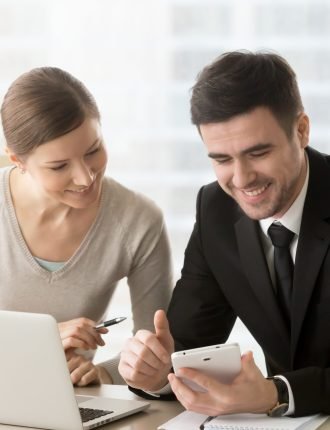 Smiling businessman presenting promising project concept with digital tablet in hand to interested businesswoman during meeting or negotiation. Female and male coworkers working together at office